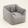 A light grey quilted raised dog car booster seat photographed from a three-quarter angle, empty, showing the tether clip on a warm cream background.