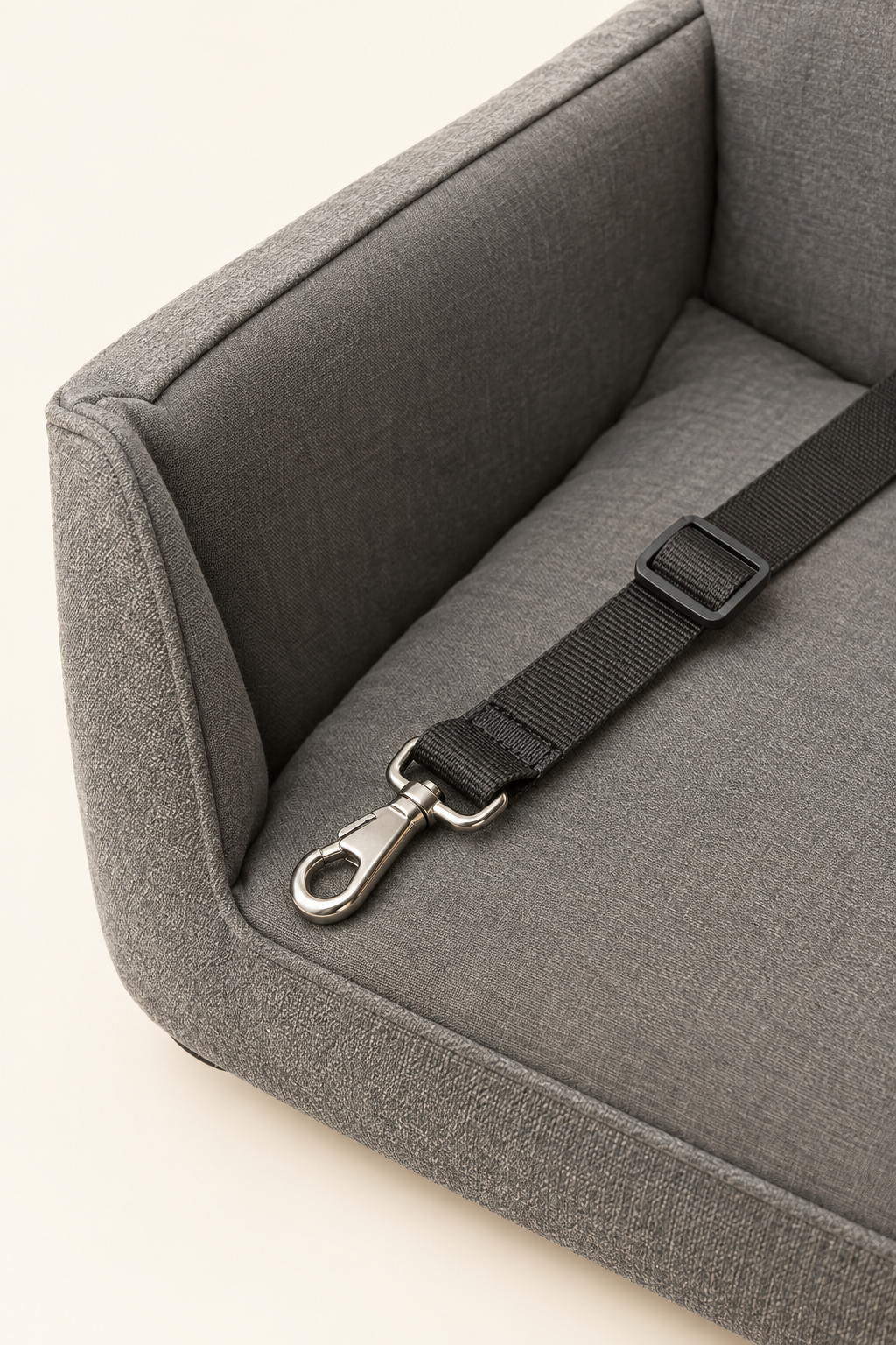 A close detail crop of the safety tether clip and adjustable strap on a grey dog car booster seat on a warm cream background.