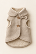 A soft oatmeal fleece-lined pet coat laid flat showing the wooden button fastening and small fabric bow on a warm cream background.