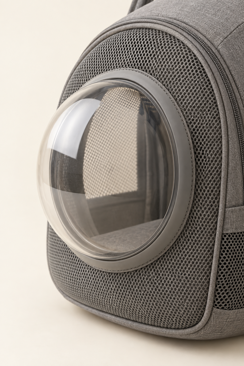 A close detail crop of the clear bubble window and its surrounding mesh on a grey pet carrier on a warm cream background.