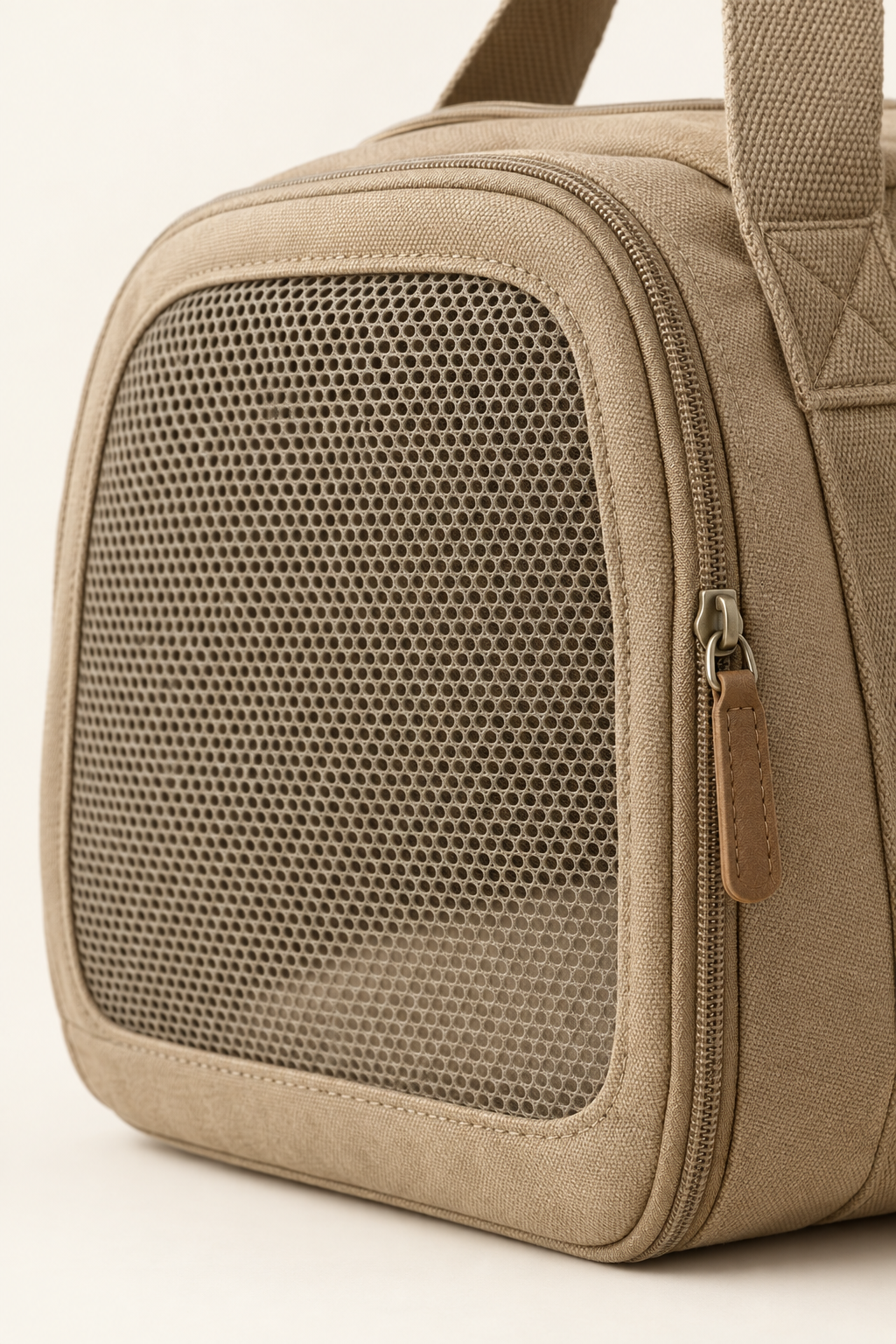 A close detail crop of the breathable mesh panel and zip pull on a tan canvas pet carrier on a warm cream background.