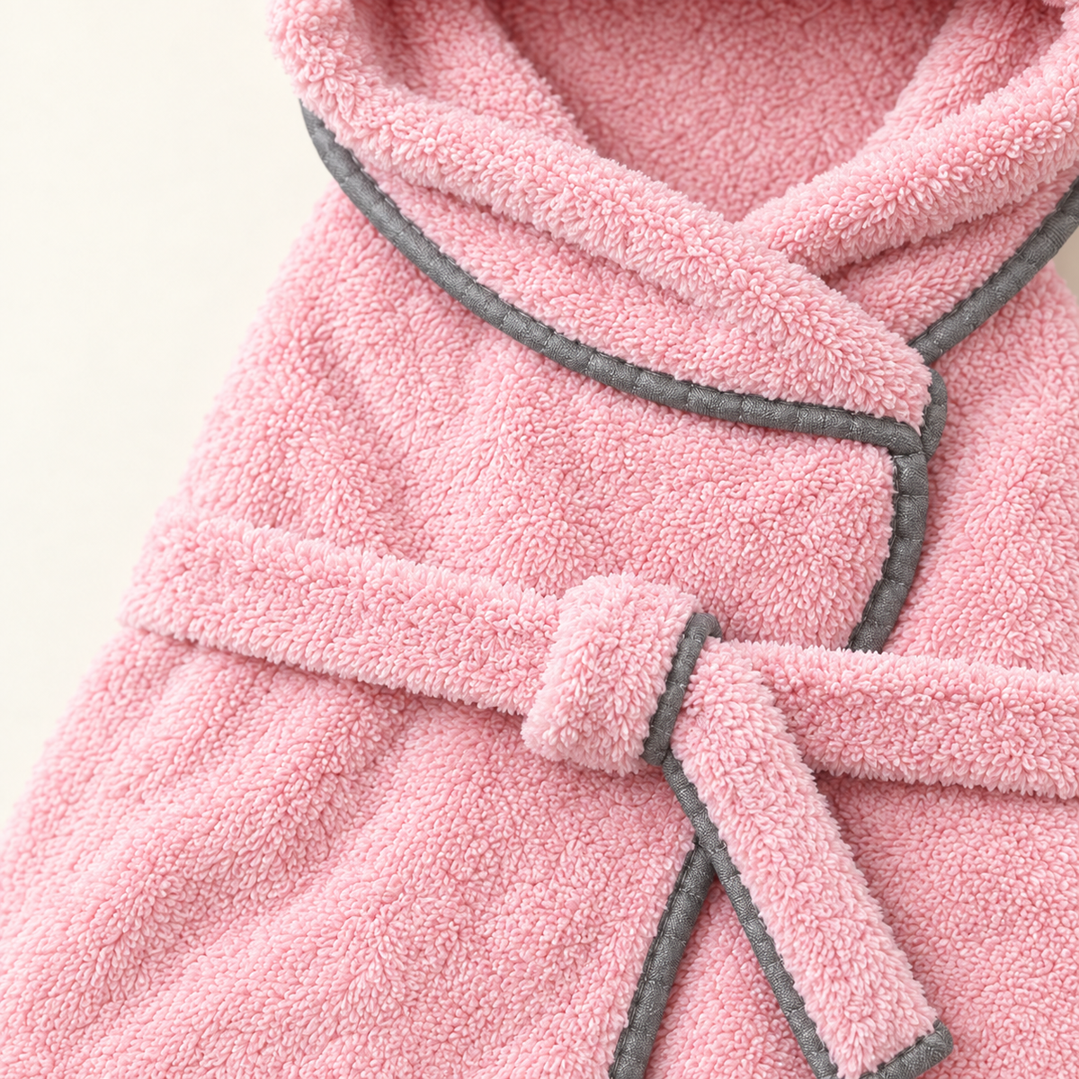 Close detail of the plush towelling pile of the pink robe, its grey bound edge and the knotted belt tie
