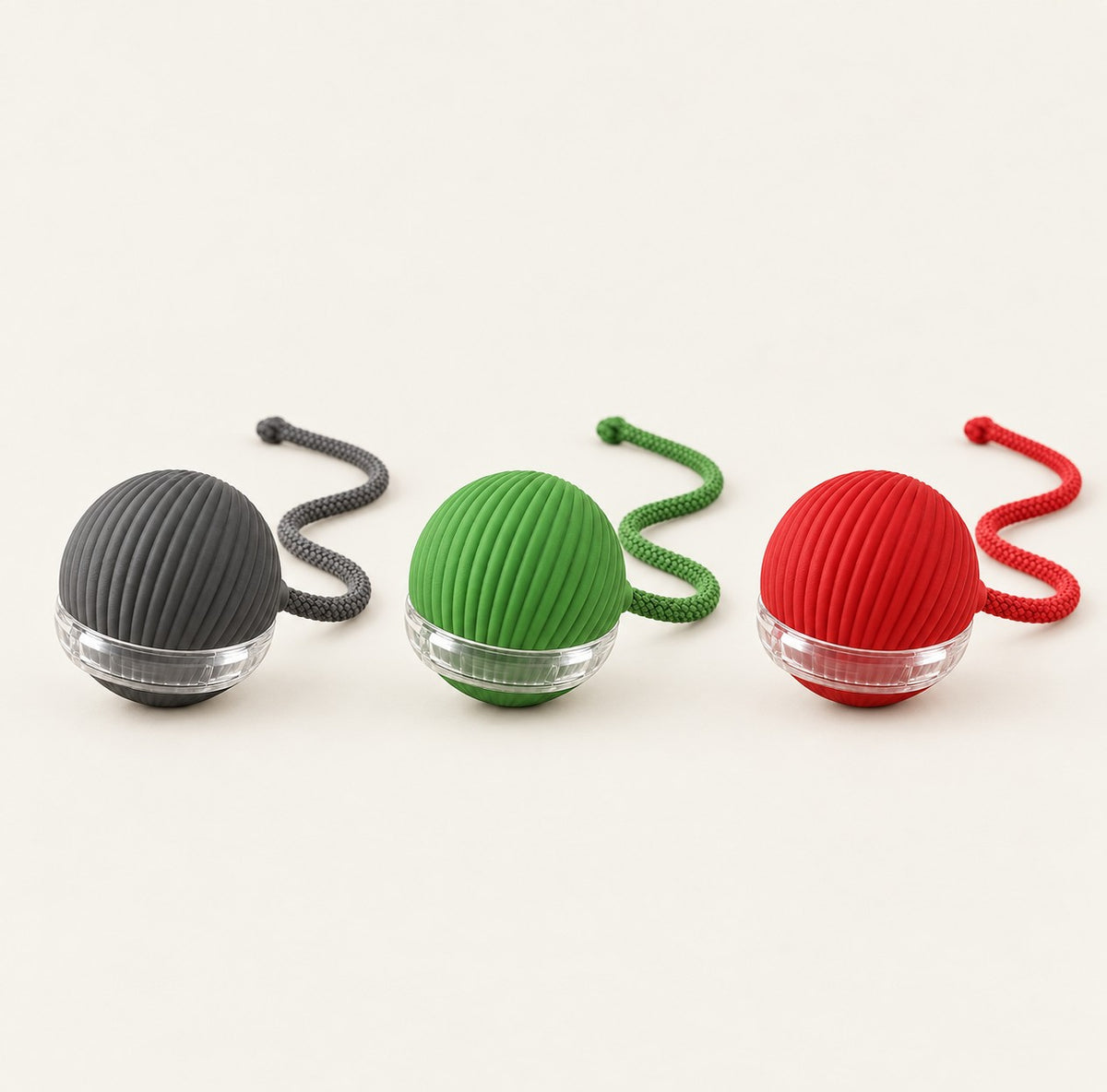 Three self-rolling ball cat toys in a row: grey, green and red, each with a matching braided cord tail