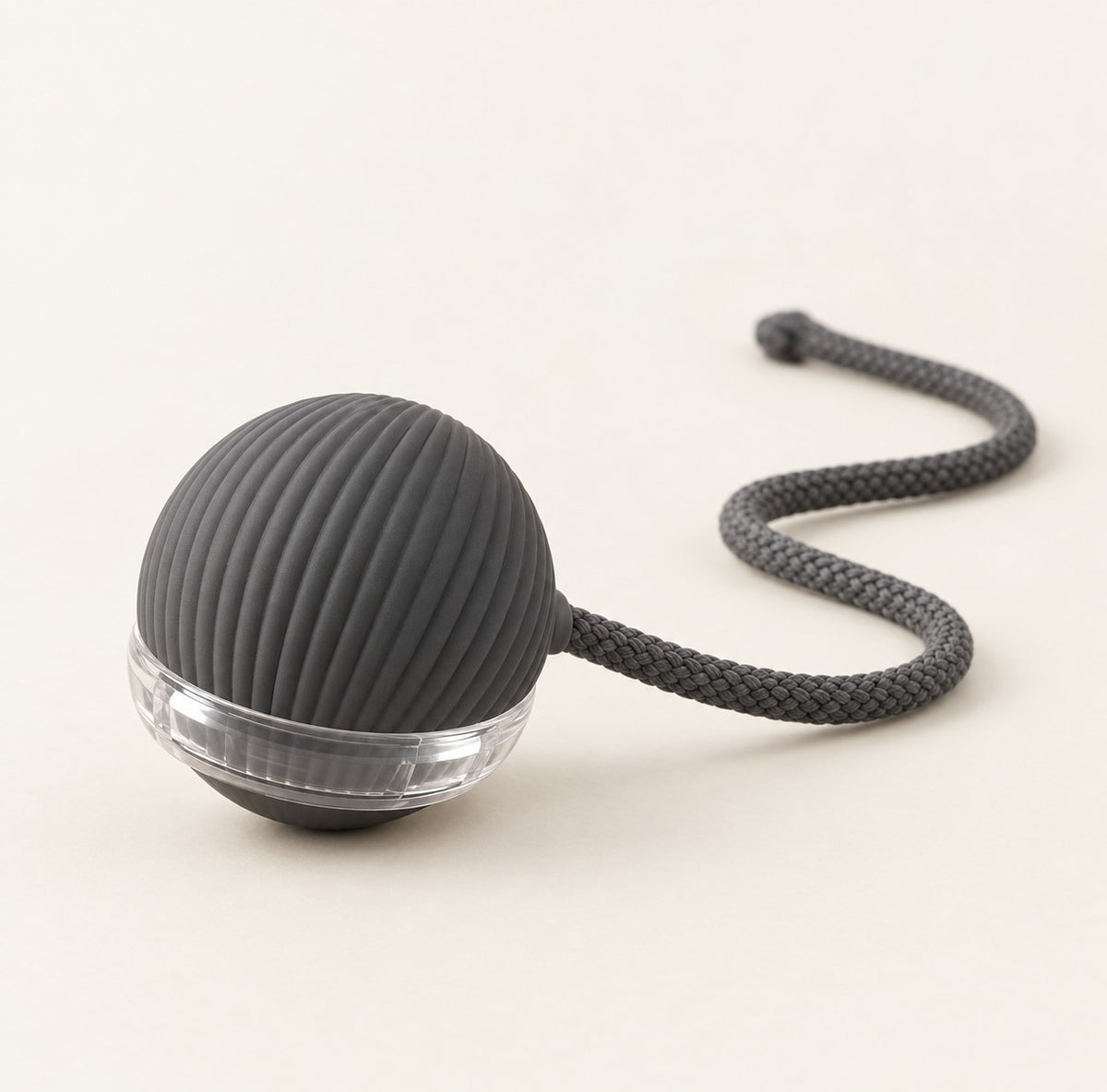 Dark grey ribbed silicone self-rolling cat toy ball on a clear plastic band, with a braided cord tail trailing behind