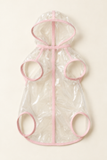 A clear transparent dog rain poncho with soft pink trim, laid flat to show the hood and leg openings on a warm cream background.