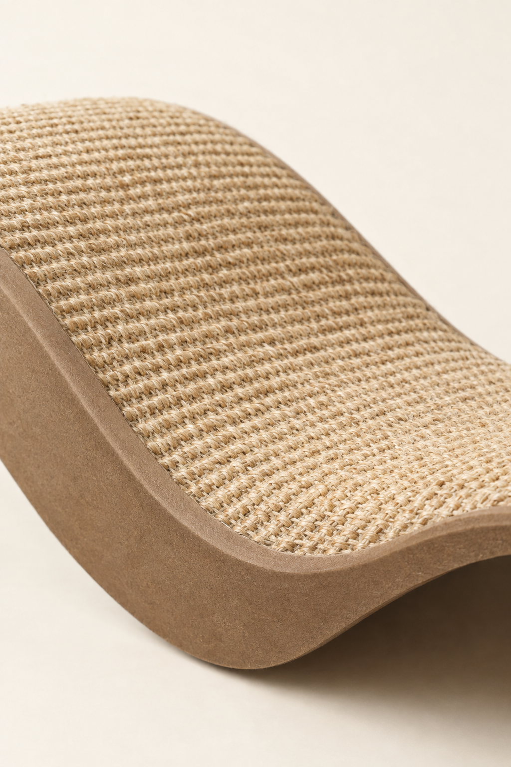 A close detail crop of the woven sisal scratching texture on a curved cat scratcher on a warm cream background.