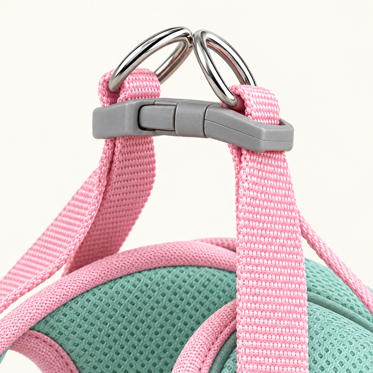 Close detail of the grey side-release buckle and the metal D-ring on top of the harness, with the pink webbing straps