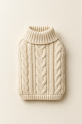 A cream knitted pet sweater laid flat and neatly folded, showing the ribbed collar and cable knit texture on a warm cream background.